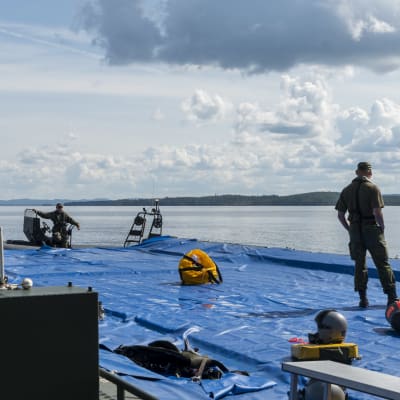 Hävittäjälentäjän ja Pilatus-yhteyskoneen pelastuslautat sekä puolustusvoimien henkilökuntaa ponttoonisillalla. 