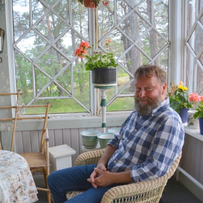 Berndt Ardell är en man med skägg och blå-vitrutig skjorta. Han sitter i en korgstol på verandan.