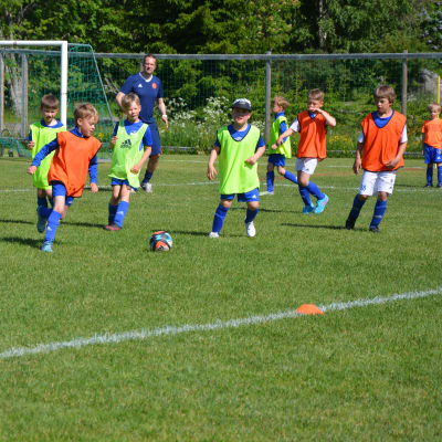 Fotbollsjuniorer med gula och orangea neonvästar spelar fotboll mot varandra. 