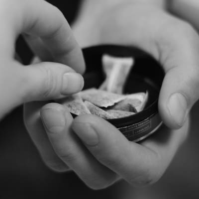 En hand tar en prilla snus från en dosa som en annan person håller fram.