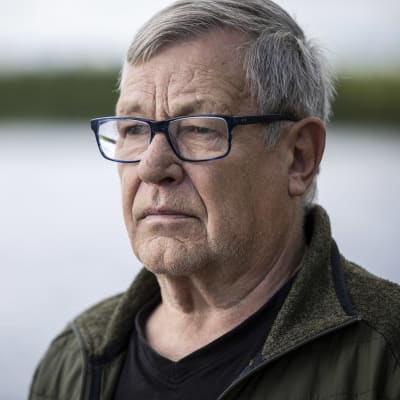 Silmälasipäinen mies ja taustalla vesistöä. 