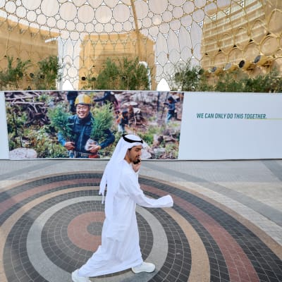 En man går förbi klimatmötesskyltar på mässcentret där mötet ska hållas i Dubai.