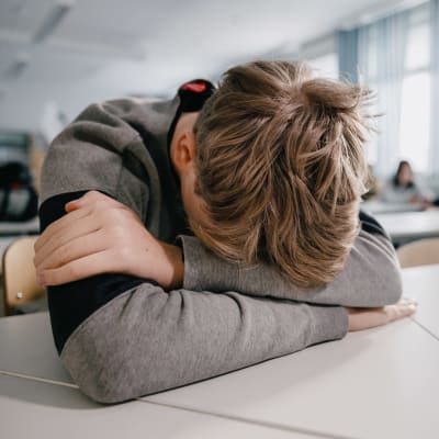 En elev lutar sitt huvud mot ett bord i ett klassrum.