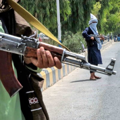 Kaksi Taliban-taistelijaa seisoo tiellä. Kuvassa etualalla on toisen taistelijan pitelemä rynnäkkökivääri.