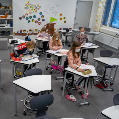 En skolklass med andraklassare sitter vid sina pulpeter. Alla har munskydd.