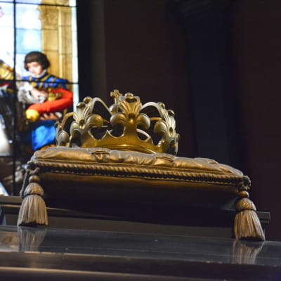 En förgylld krona framför ett målat kyrkglas.