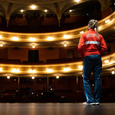 Auri Ahola fotograferad bakifrån på scenen i Nationalteatern framför tomma läktare..