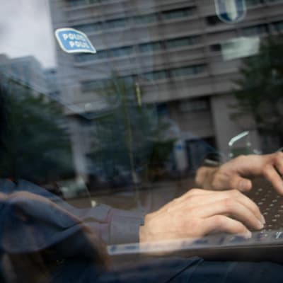 En polis knäpper på ett tangentbord. Bilden är tagen utanför ett stängt bilfönster.