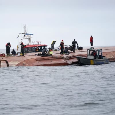 Dykare och andra räddningsarbetare står på det kapsejsade fartyget Karin Hoej.