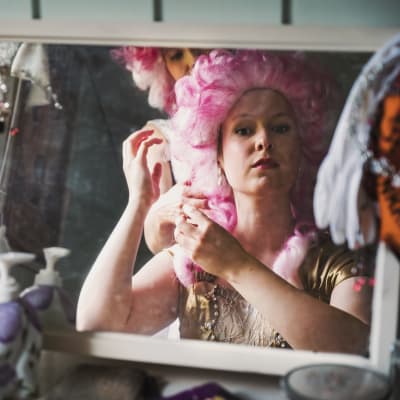 Pianisti Sonja Hendunen katsoo peiliin pinkki perukki päässä, taustalla laulaja Noora Määttä.