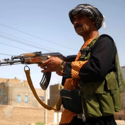 Två beväpnade afghanska milismän. I bakgrunden syns en mur och ett hus.
