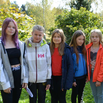 Sex glada 12-åringa flickor står bredvid varandra på en skolgård. 
