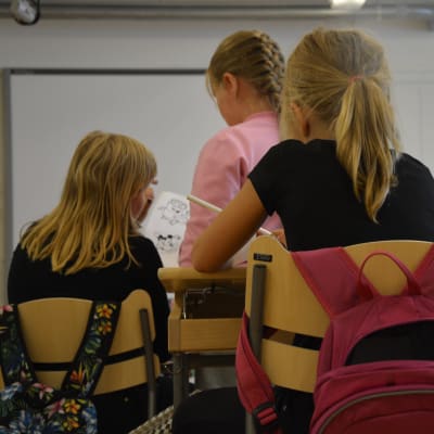 Ryggen på en handfull elever vid sina pulpeter i ett klassrum.