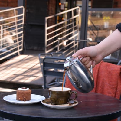 Kaffe hälls upp i en kopp bredvid en runebergstårta