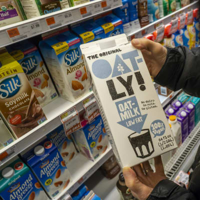 En person håller i en kartong med havremjölk av märket Oatly i den butik.