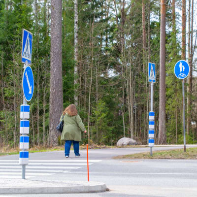 Kvinna går på övergångsställe med blinkande ljus som varnar för fotgängare.