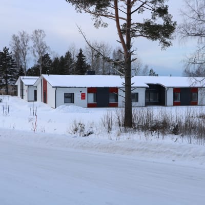 En radhus byggnad med vita och röda väggar. Framför byggnaden finns två träd.