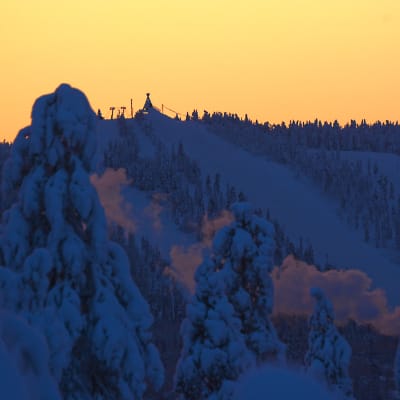 Ounasvaaran hiihtokeskus näkyy lumisten puiden takaa, punertava taivas.