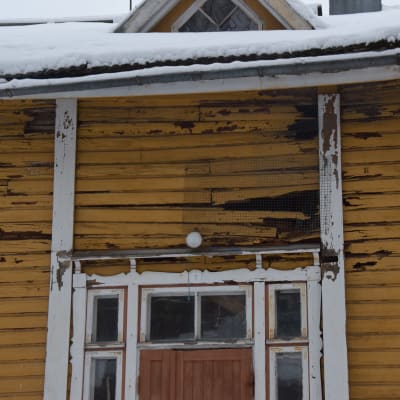 En gul trävilla, gammal arbetarbostad med fler bostäder. Målfärgen flagar, stockarna är ruttna vilket lett till hål i ytterväggarna.