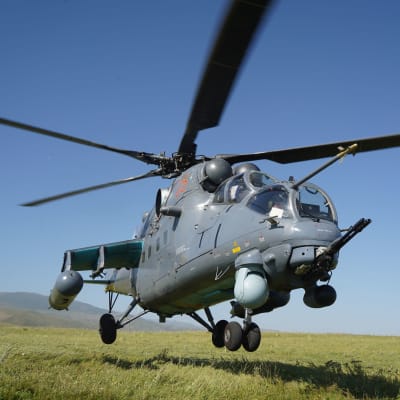 En militärhelikopter av modellen Mi-35M i närbild ovanför en grässlätt.