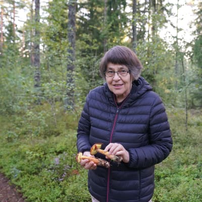 En kvinna står i skogen med svampar i sina händer.