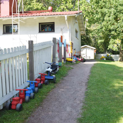 En bild på en gård där barntrampbilar står uppradade längsmed ett staket. På bilden syns hus och gräs