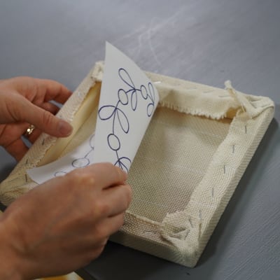 Händer sätter mönsterpapper inne i tuftningsramen