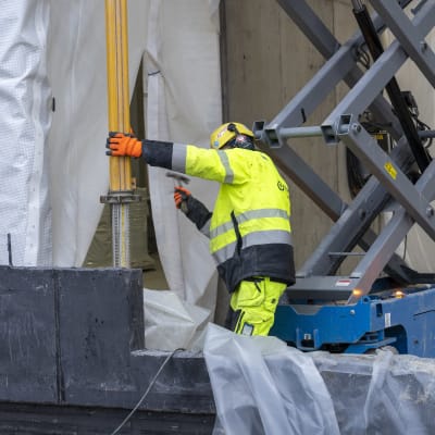 Konalaan valmistuvan Helsingin pelastuslaitoksen työmaa, talon runko pystyssä, etualalla työmies vasaroi.