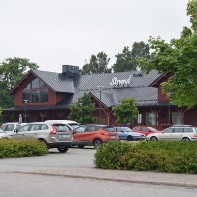 Köpcentret Strand i Ingå. Framför byggnaden står bilar parkerade på en parkering.