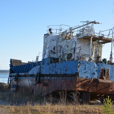 En gammal och rostig båt står på land.