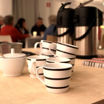 I förgrunden kaffekoppar, i bakgrunden deltagare i vänskapskaféet i Luckan i Helsingfors.