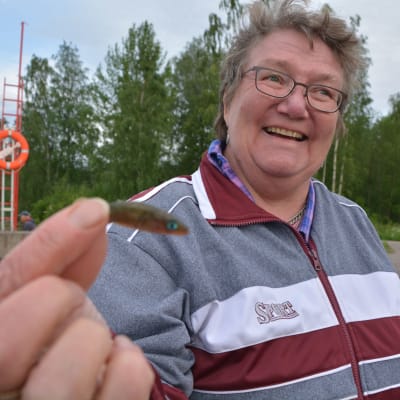 Kvinna håller upp en pytteliten fisk som hon fångat md håv.