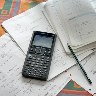 En miniräknare, papper och en matematikbok på ett bord.