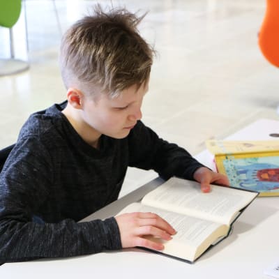 En pojke sitter och läser i en bok. 