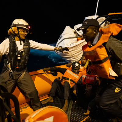 Pelastustyöntekijä ojentaa kättä miehelle kumiveneessä.