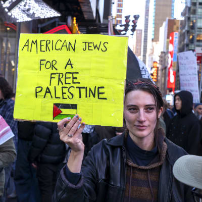 En ung kvinna håller upp en gul skylt där det står "Amerikanska judar står för ett fritt Palestina". I bakgrunden syns fler demonstranter.