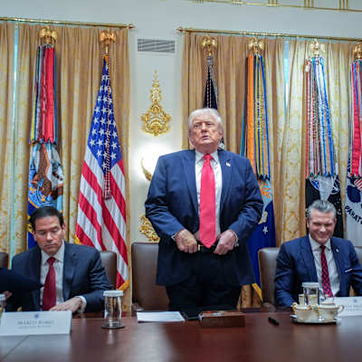 Donald Trump seisoo pidellen housujensa vuotä kaksin käsin. Vieressä pöydän ääressä istuu Marco Rubio ja Pete Hegseth.