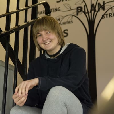 Kaisla Kauppinen istuu kierreportailla ja katsoo hymyillen kameraan.