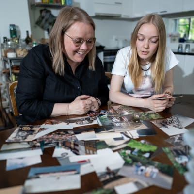 Äiti Reija Jyrkinen (vas) ja 16-vuotias tytär Kaisa Jyrkinen tutkimassa Reijan vanhoja Interrail-häämatkan valokuvia perheen keittiönpöydän ääressä.