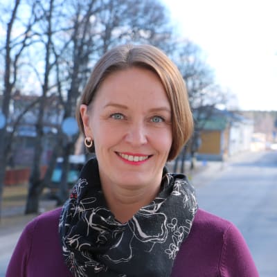 En kvinna i 40-årsåldern med kort mörkt hår. I bakgrunden syns en gata och träd.