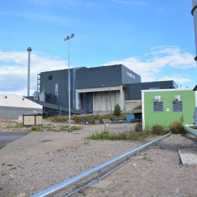 En svart byggnad med en grön container i förgrunden.
