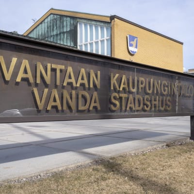 Enskylt med texten Vanda stadshus. i Bakgrunden syns stadshuset med kommunvapnet på väggen.