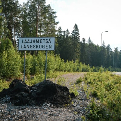 En asfalterad väg i en skog och en skylt där det står Laajametsä/Långskogen.