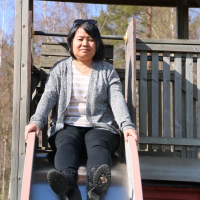 En asiatisk kvinna i 50-årsåldern sitter i en rutschkana.
