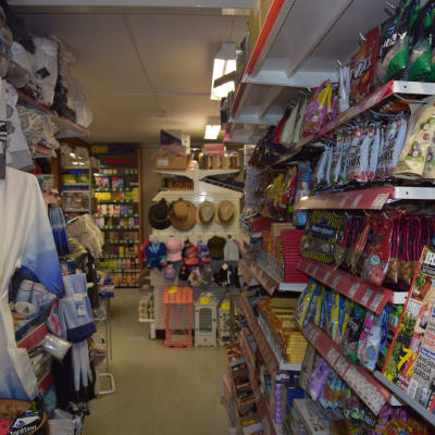 En smal gång i en butik. Mycket varor, bland annat tidningar, godis och kläder på båda sidor av gången.