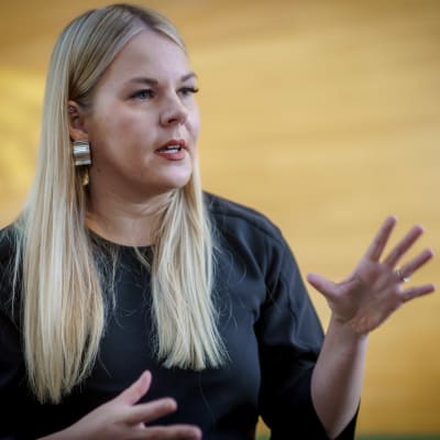 Europaparlamentarikern Alviina Alametsä står framför en gul vägg. Hon har ena handen i luften och spretar med fingrarna.