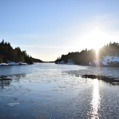 Vinterkväll i inre farleden i Barösund med solen som går ner över Bergvalla. Havet är öppet med enstaka simmande isflak.