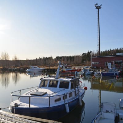 Några båtar som ligger vid Isnäs hamn på hösten då det redan ligger lite snö på bryggan. Vattnet är stilla och solen skiner.