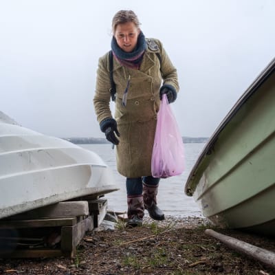 Nainen kerää roskia rannalla soutuveneiden välissä. 