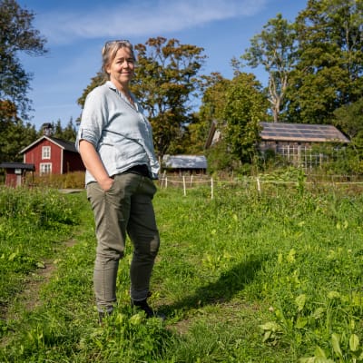 Jordbrukaren Nina Långstedt vid en åker, med gården i bakgrunden. 